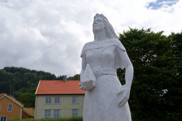 The statue of St. Sunniva at the harbor in Selje. Prestegarden Pilgrim Center in the background.
